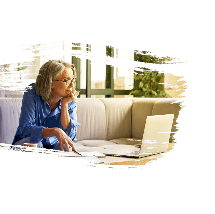 A woman sits on the couch using her laptop.