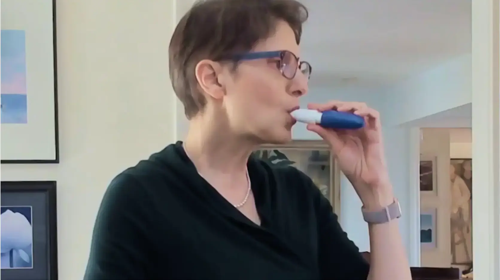 A woman with glasses holds the INBRIJA inhaler to her mouth. Text on the bottom right of image reads "Bettina’s Story"